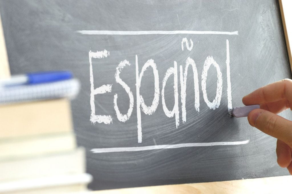 Hand writing on a blackboard in a language class with the word "Spanish" written on it. Some books and school materials.
